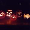 A row of lit pumpkins glowing in the night, carved to resemble the Batman symbol, Harry Potter, a cat, a funny face and a spooky face