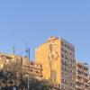 The sun shines majestically on the side of a building in Amman, illuminating the mural of a man bearing the crown of a pillar on his head 