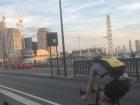 A bicyclist crosses a bridge, with a red London bus in the background