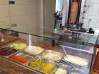 Meat roasting on a spit behind a counter where various ingredients are sitting