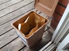 A small brown bin containing compost materials standing on a porch