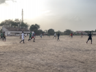 The students play football on a sandy field after school