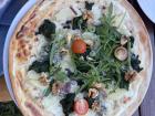 A round flammkuchen at a restaurant with tomatoes, spinach, walnuts and peaches