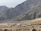 Our expedition vehicles parked near a snow leopard spotting site, surrounded by towering cliffs and open slopes