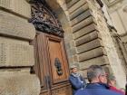 The tour guide knocks on the door with the group to enter the building