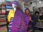Storeowner in Lagos holds woven fabric that shimmers because of sparkly thread. 