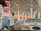 A driver refueling at a local gas station with a long line of cars behind. The car's windshield was shattered. With no air conditioning, it was sweltering!