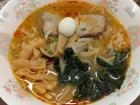 The bowl is topped with a quail egg, bamboo shoots, spinach and slices of pork