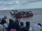 Boats off the beach waving Garifuna flags while visitors watch. 