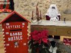 Babbo Natale (Santa Claus) sitting next to a mailbox that says "Lettere a Babbo Natale" which means "Letters to Father Christmas/Santa Claus"