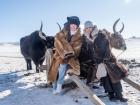 My friend and I wearing animal fur to stay warm in the windy cold while sitting on a cart pulled by yaks