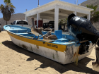 A fishing boat at the beach guarded by many large pelicans