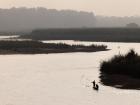 Fishermen float on a river in the Terai, with one person moving the boat and the other tossing their net